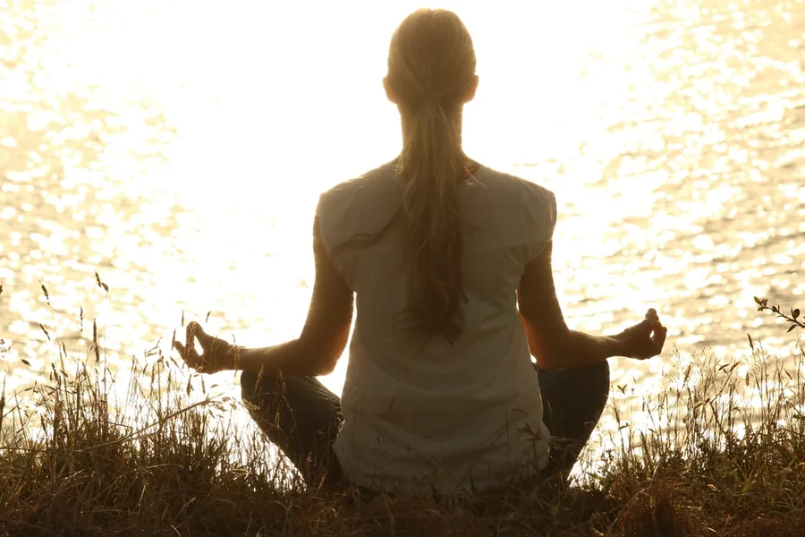 Woman meditating by the water in the light of early morning