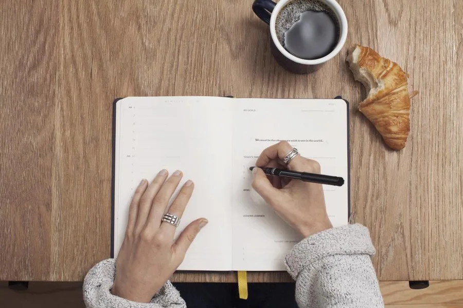 Hands writing morning pages in a journal beside a cup of coffee