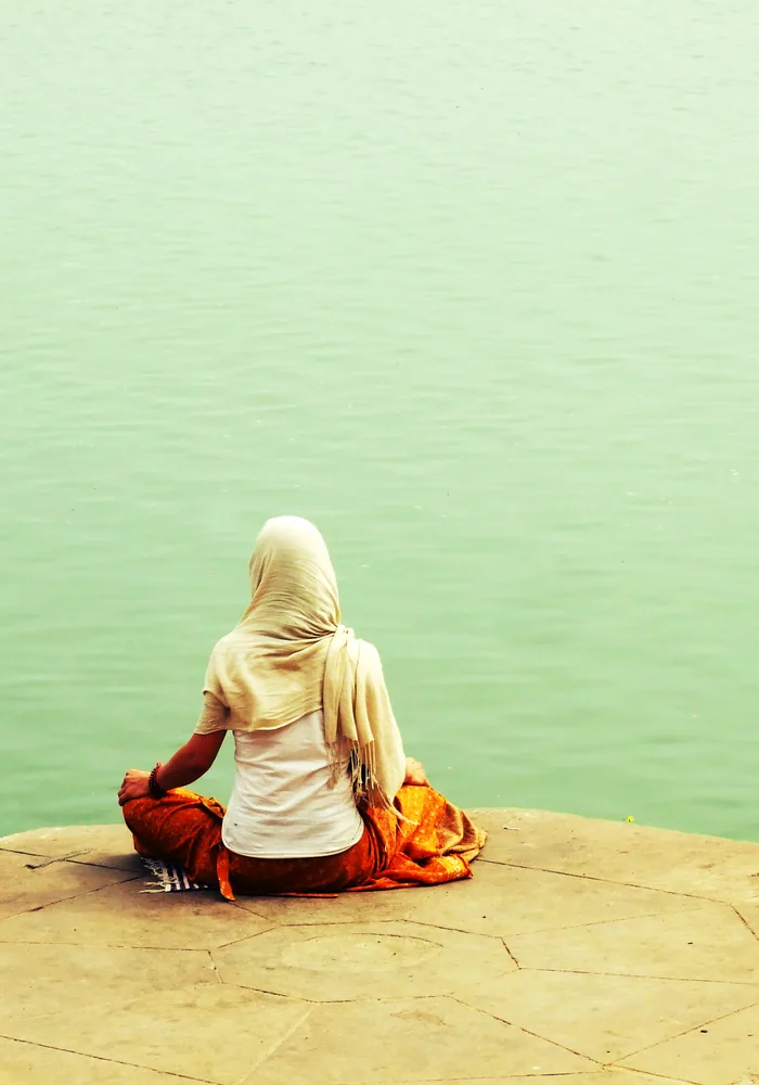 Person sitting cross-legged by a river in quiet meditation