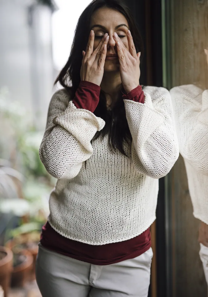 Tired woman standing by a window with her hands over her eyes