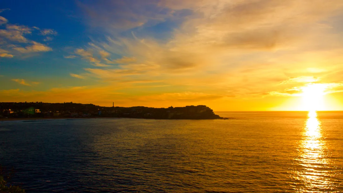 Wide sunset over a calm sea and distant coastline